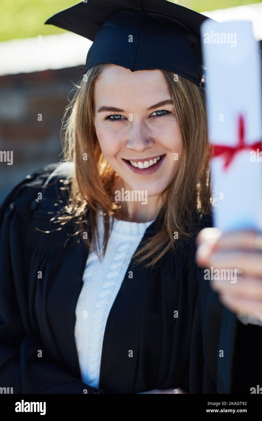 Its definitely my proudest moment. Portrait of a young student holding her diploma on graduation day. Stock Photo