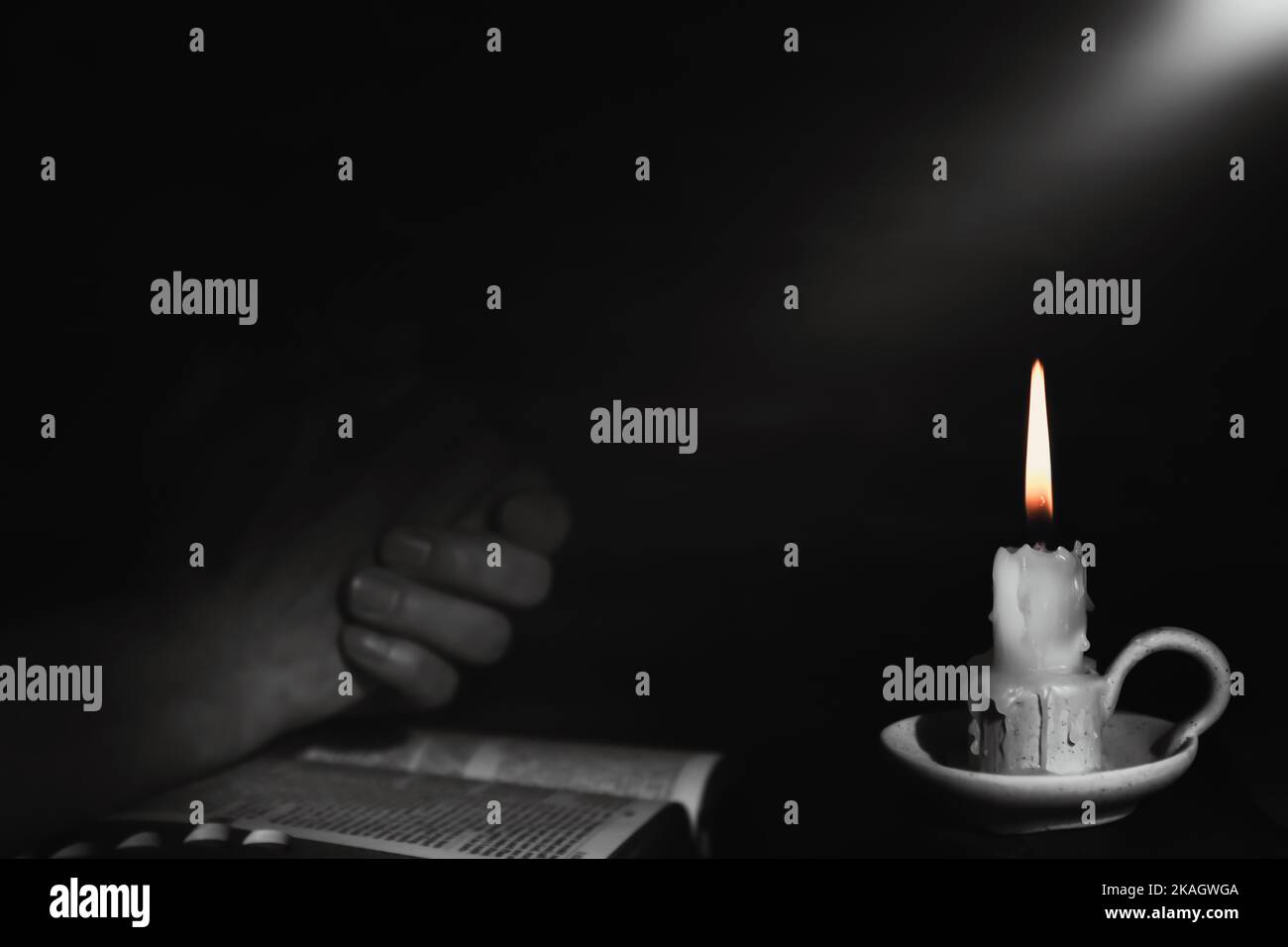 Holy bible and praying man's hands and burning candle background with