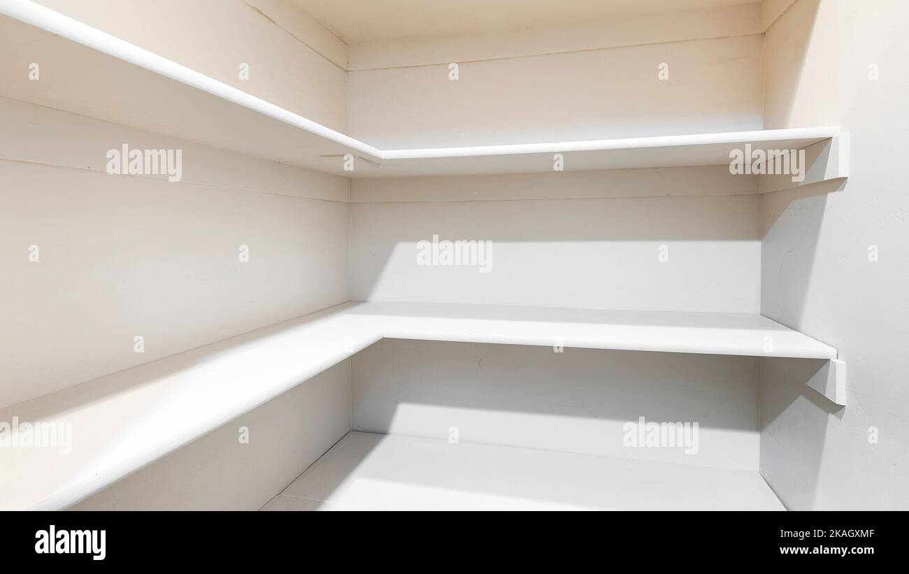 Panorama White linen closet with wall mounted shelves and carpeted floor. Narrow walkin closet