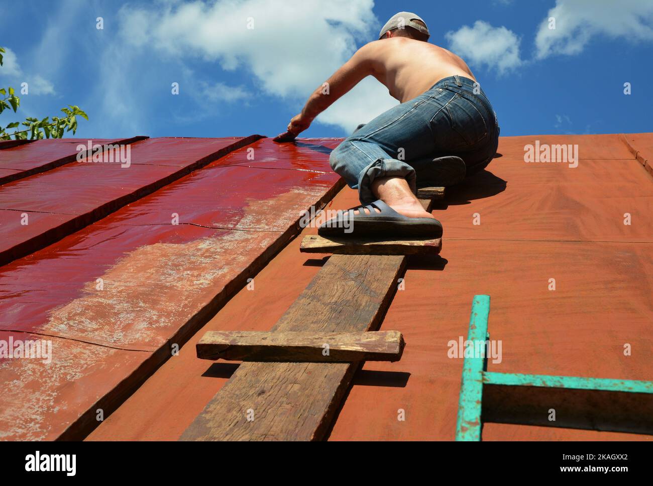 Painting old metal roof with a paint brush. Worker repainting house