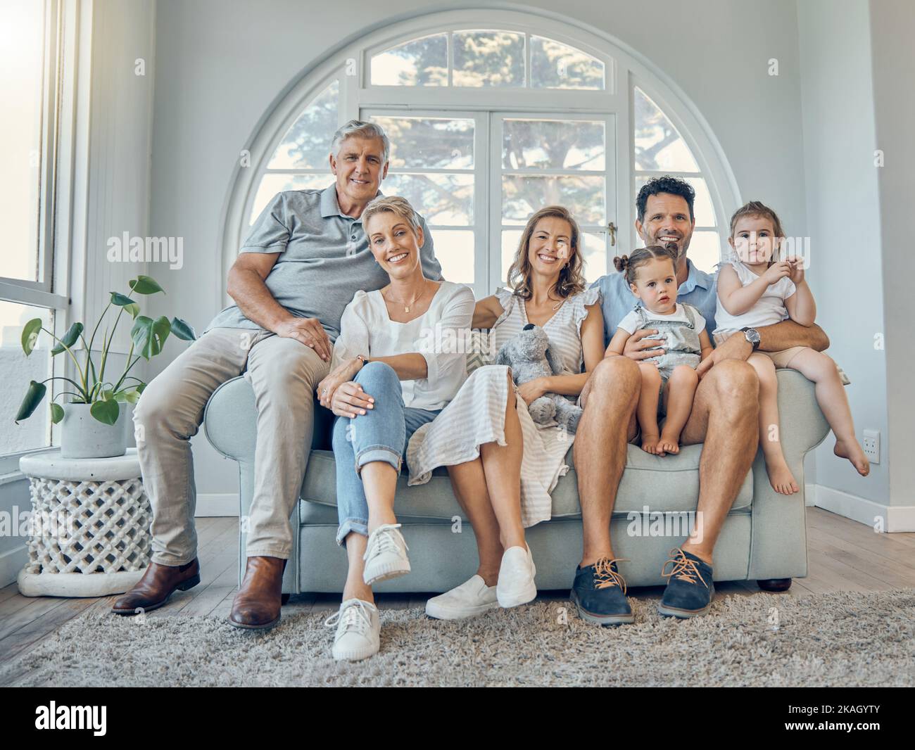 Big family, portrait and generations relax together on couch in living room at home. Happy grandparents, mother smile and father love adorable young Stock Photo
