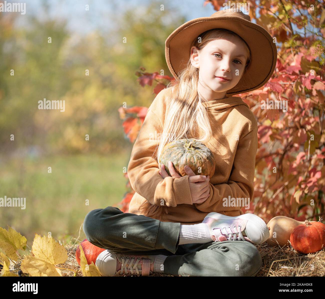 Little girls sitting among hay bales and pumpkins in the autumn garden ...
