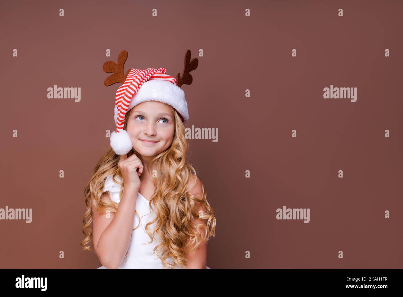 Photo funny curly girl dreaming that Christmas will bring peace and love to all people on earth looking for an empty space, wearing headdress with horns, concept christmas and new year on background Stock Photo