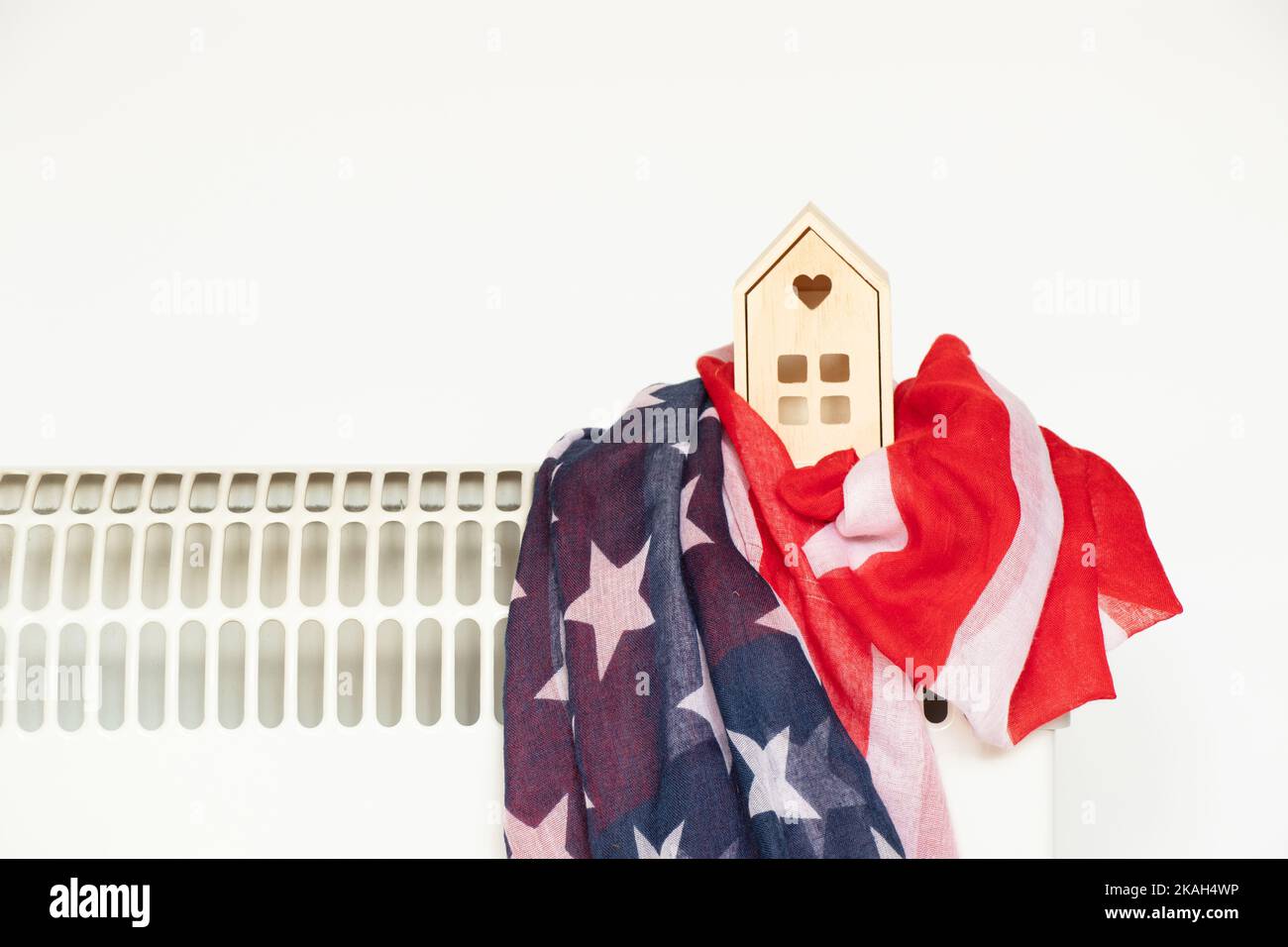 A small wooden house and the flag of America lies on a heating convector on a white background, a warm house in America, the heating season Stock Photo