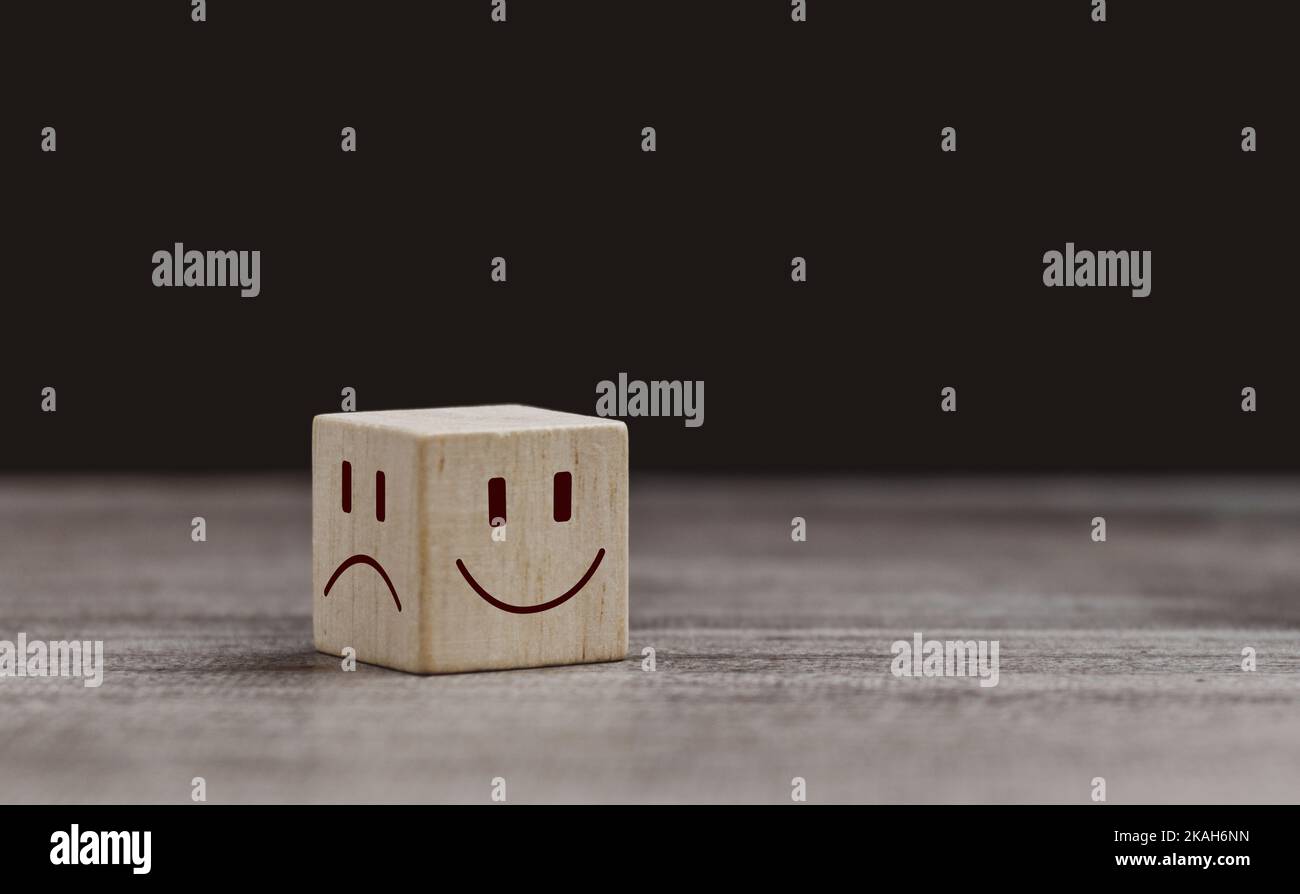 Mental health and emotional state concept, Smile face in bright side and sad face in dark side on wooden block cube for positive mindset selection. Stock Photo