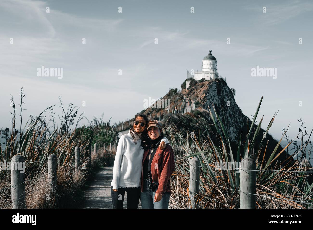two caucasian girls in white sweater and red jacket hugging each other looking at camera happy and smiling on the path leading to the beautiful Stock Photo