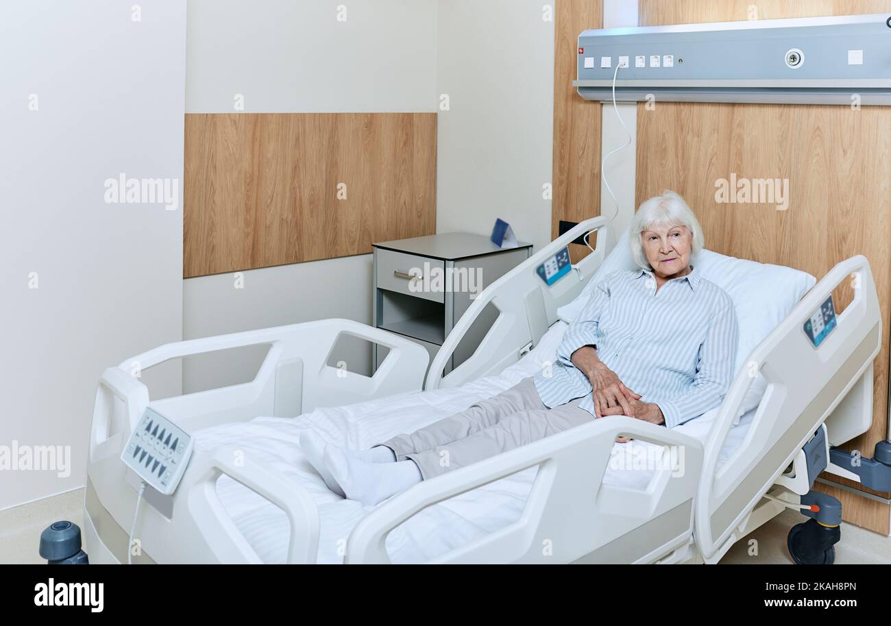 Gray-haired elderly woman lying in bed medical in ward of a modern hospital while treatment. Care and treatment of elderly people Stock Photo