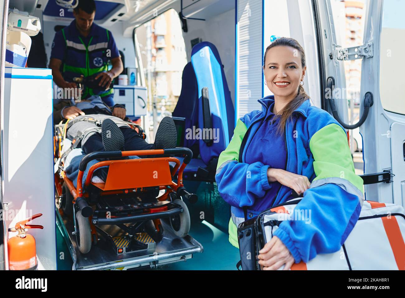 Portrait of female paramedic standing near ambulance vehicle with aid kit bag and looking at camera. Ambulance medical technician Stock Photo
