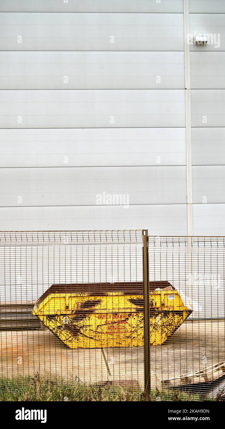 Yellow skip behind steel fence infront of grey wall Stock Photo