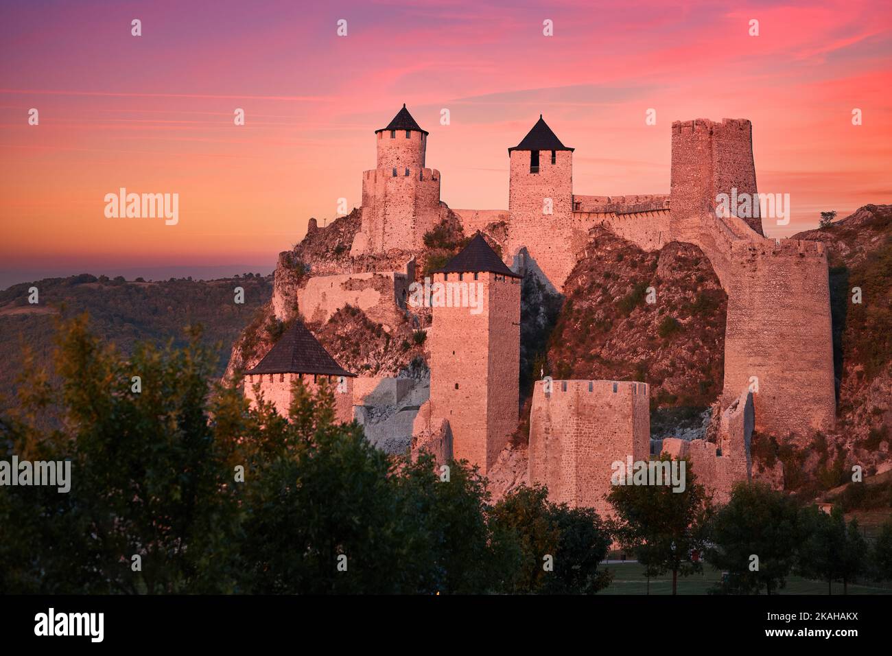 The medieval fortress of Golubac illuminated of pink light of setting sun against colorful clouds in background. Famous tourist place, Serbia. Stock Photo