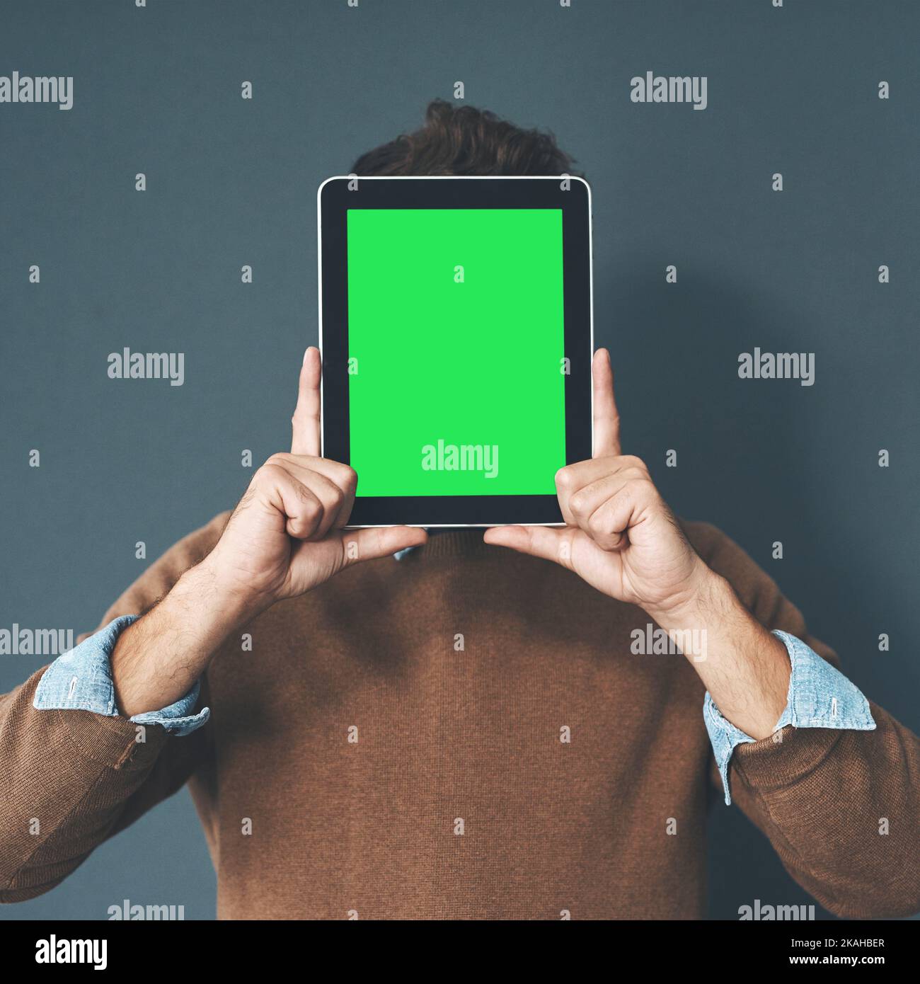 This app is the star of the show. Studio shot of a young man holding a digital tablet with a green screen against a grey background. Stock Photo