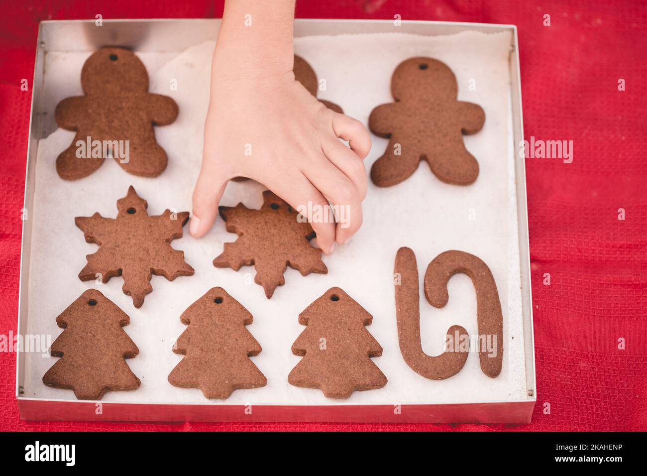 Overhead view of a child's hand reaching for a freshly baked homemade s snowflake gingerbread cookie Stock Photo