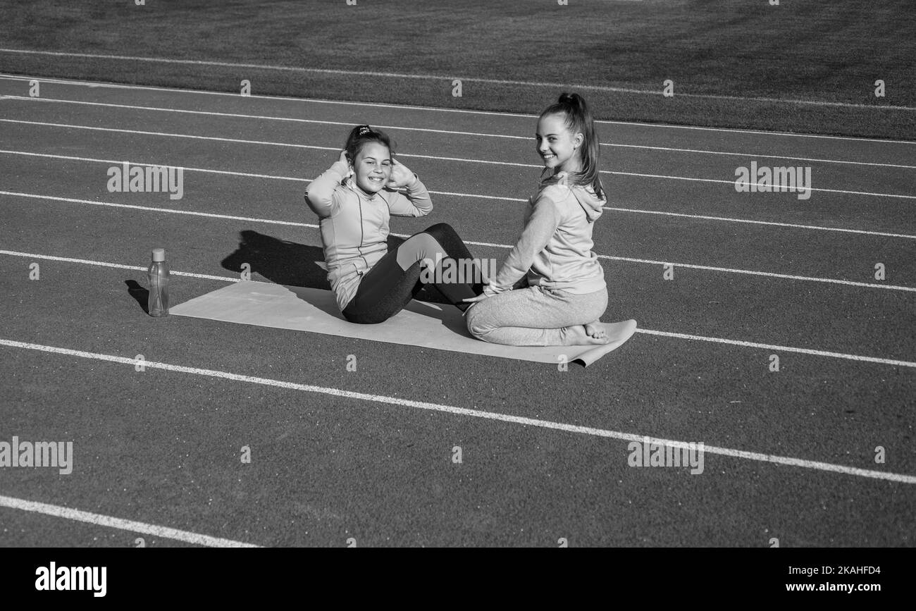 Happy fit teenage girls do situps physical training on athletics track