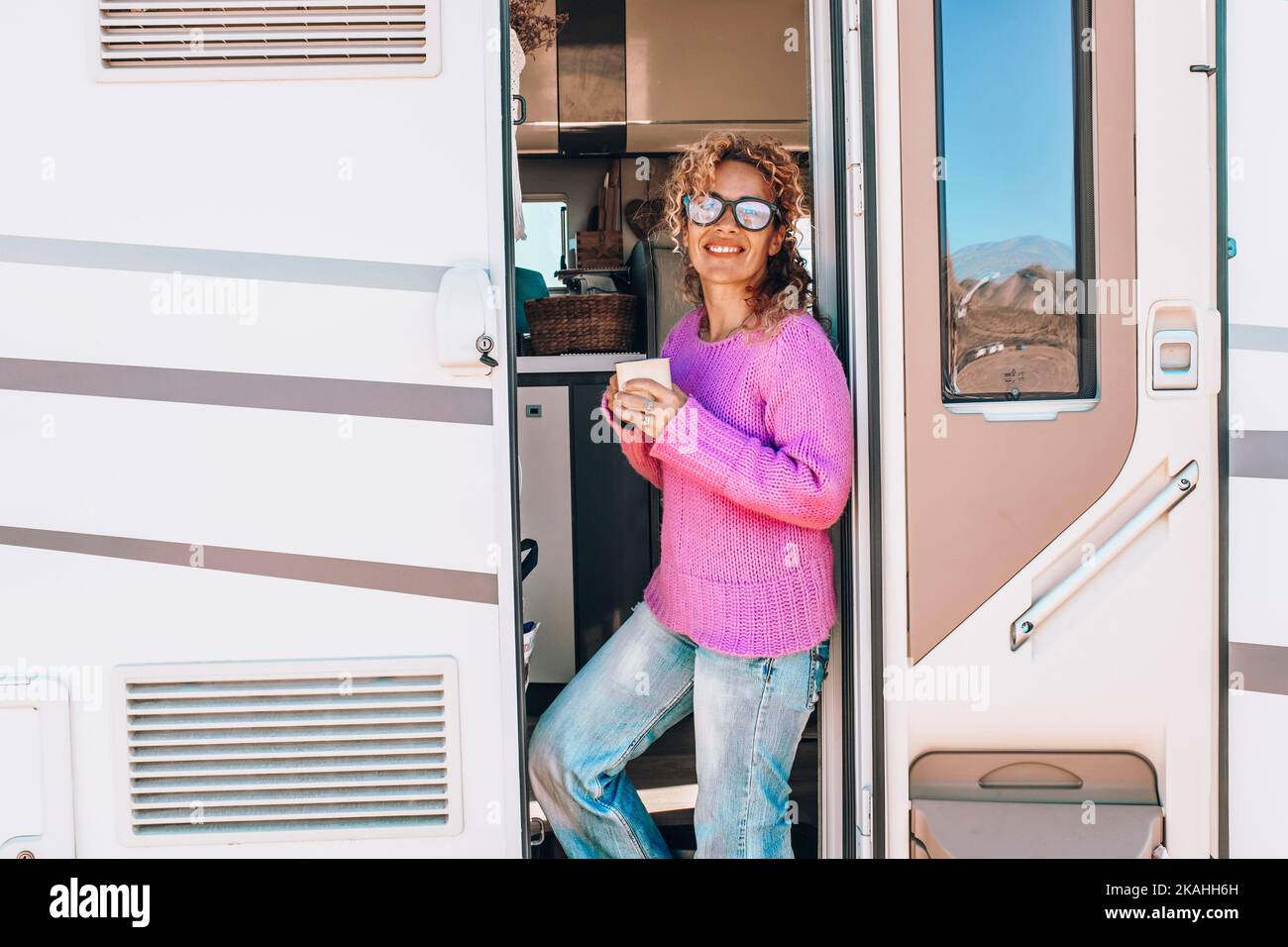 Happy female tourist standing at the door of her camper van enjoying travel and freedom destination. Pretty woman enjoy motor home van life lifestyle Stock Photo