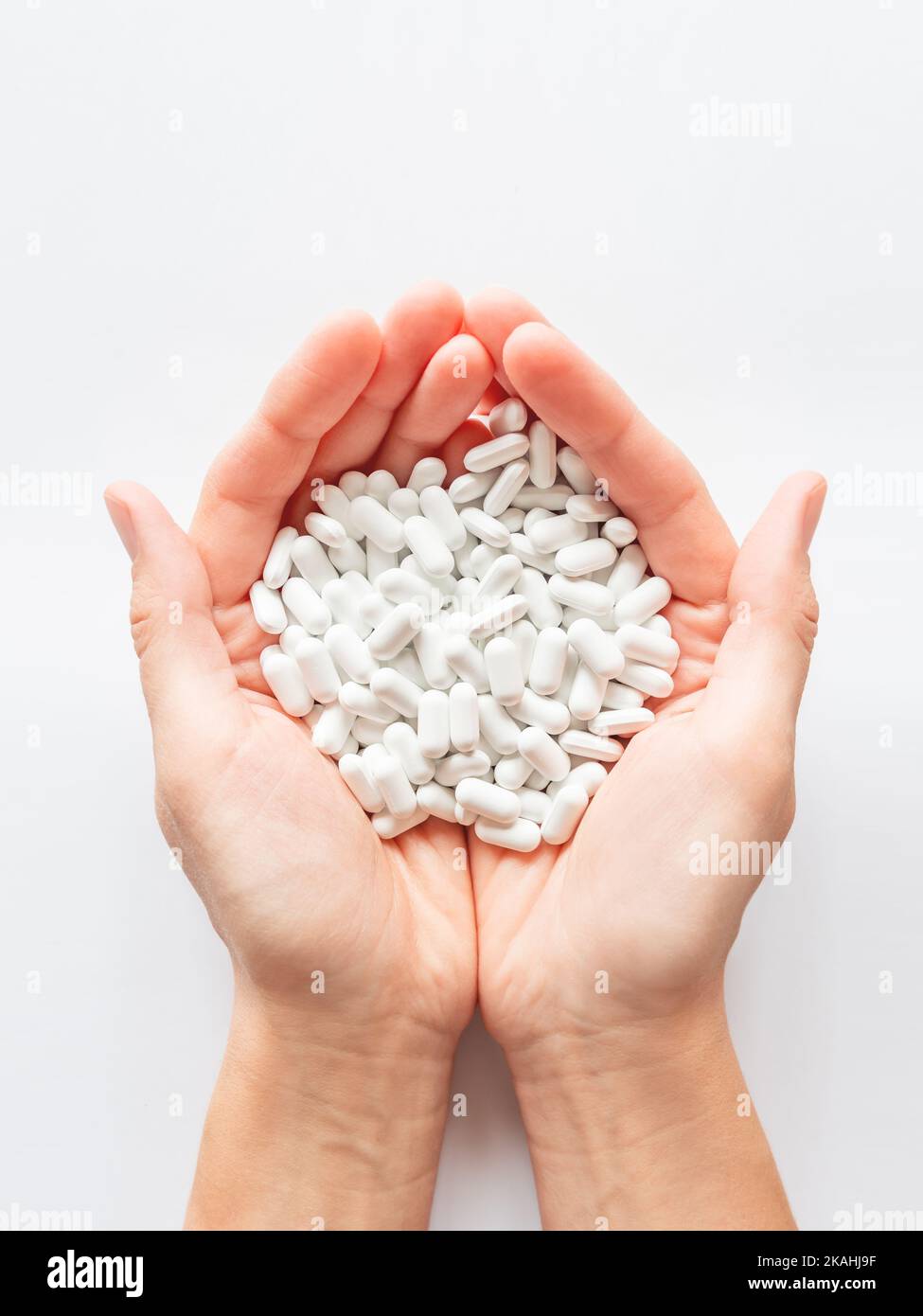 Palm hands full of white scattering pills. Woman gripes hand with capsules with medicines on light background. Flat lay, top view. Stock Photo