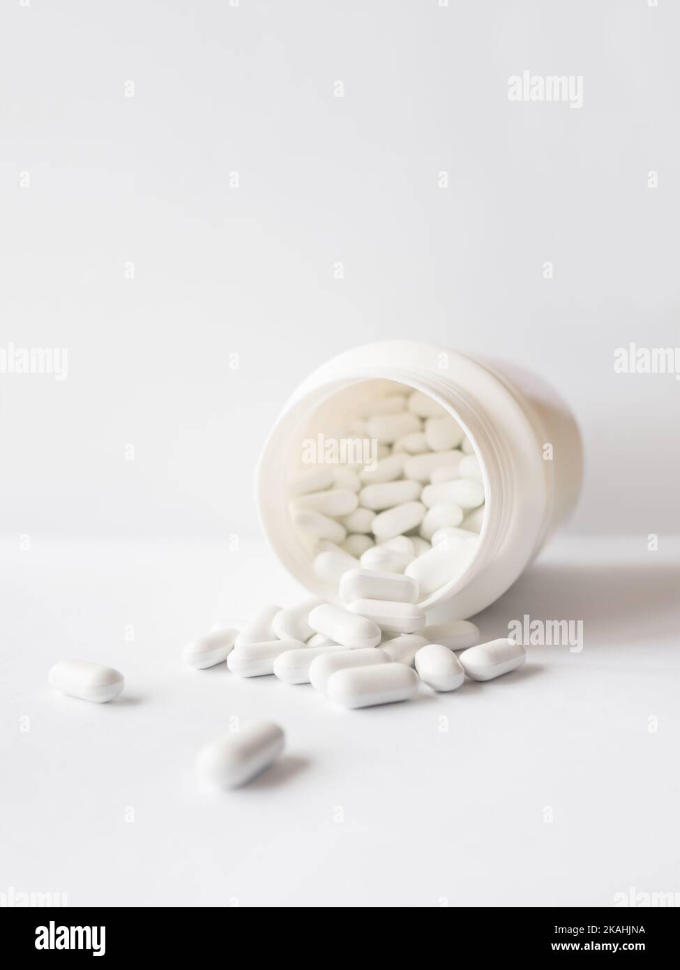 White pills spilled out of a plastic jar. Medicine capsules on white background with copy space. Stock Photo
