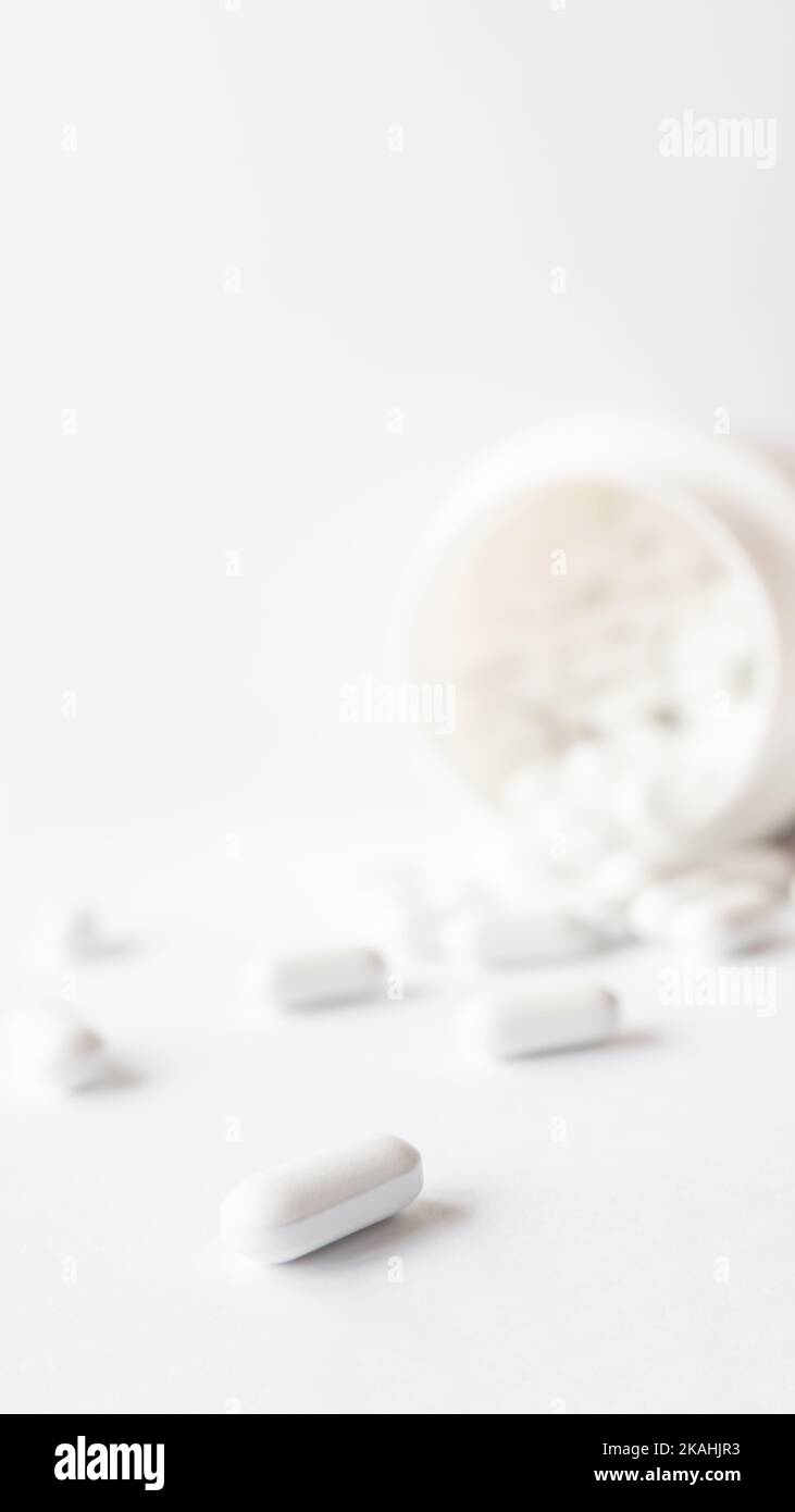 White pills spilled out of a plastic jar. Medicine capsules on white background with copy space. Stock Photo
