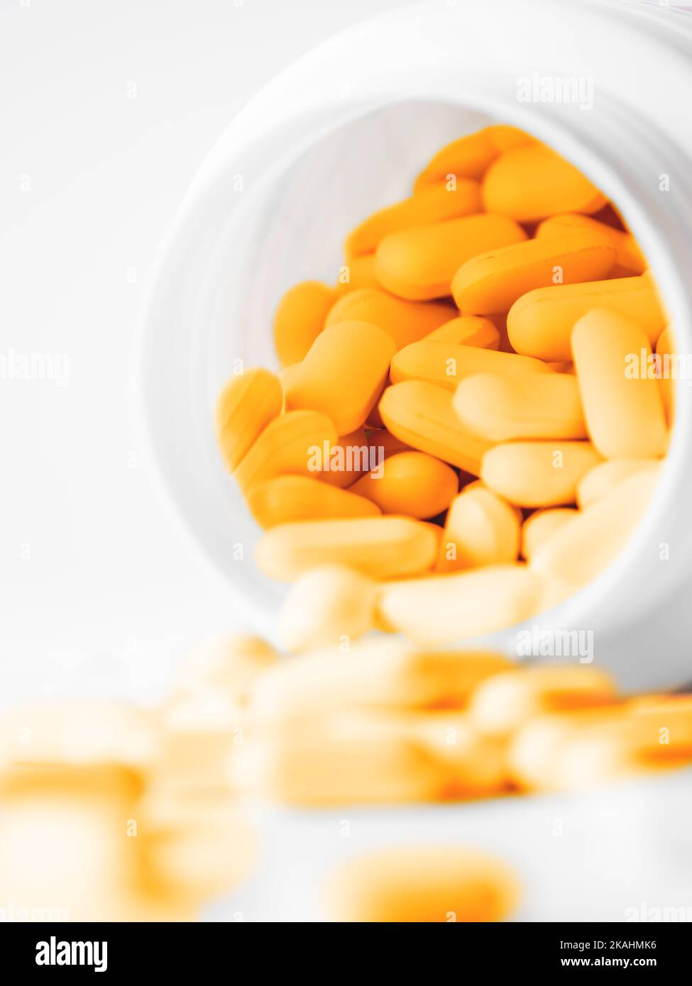 Orange pills spilled out of a plastic jar. Medicine capsules on white background. Stock Photo