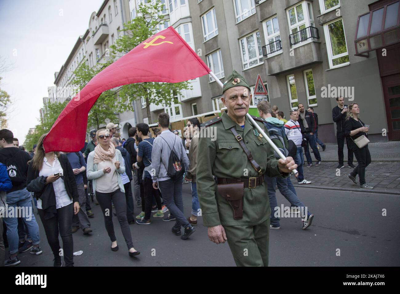 Naydencho from Bulgaria walks wearing a soldier uniform and carrying a flag of the Soviet Union during the annual MyFest in the Kreuzberg district on May 1, 2016 in Berlin, Germany. May Day, or International Workers' Day, was established as a public holiday in Germany in 1933. Since 1987 May Day has also become known in Berlin for violent clashes between police and mostly left-wing demonstrators.  Stock Photo