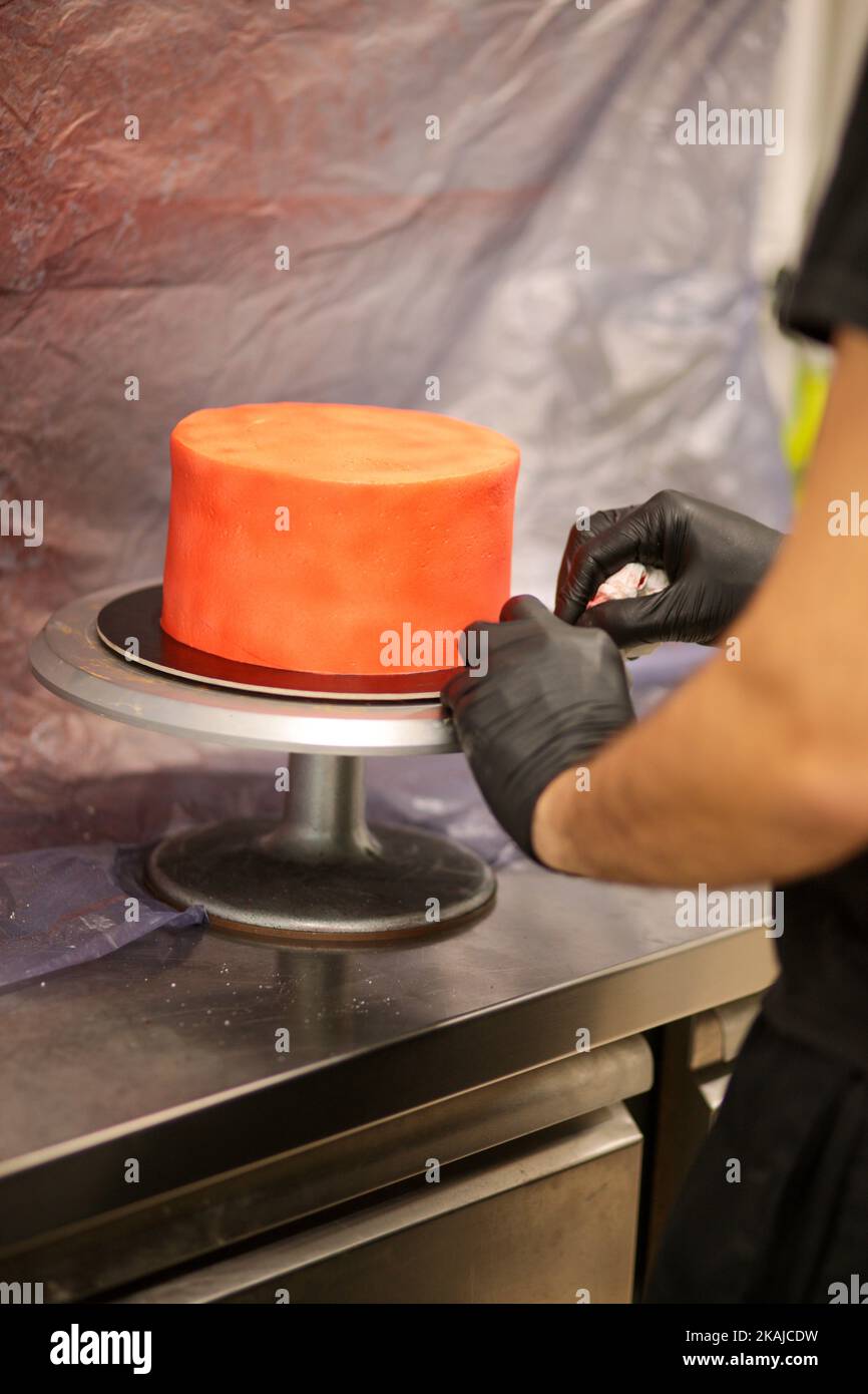 cook preparing a red frosted cake using air bush Stock Photo