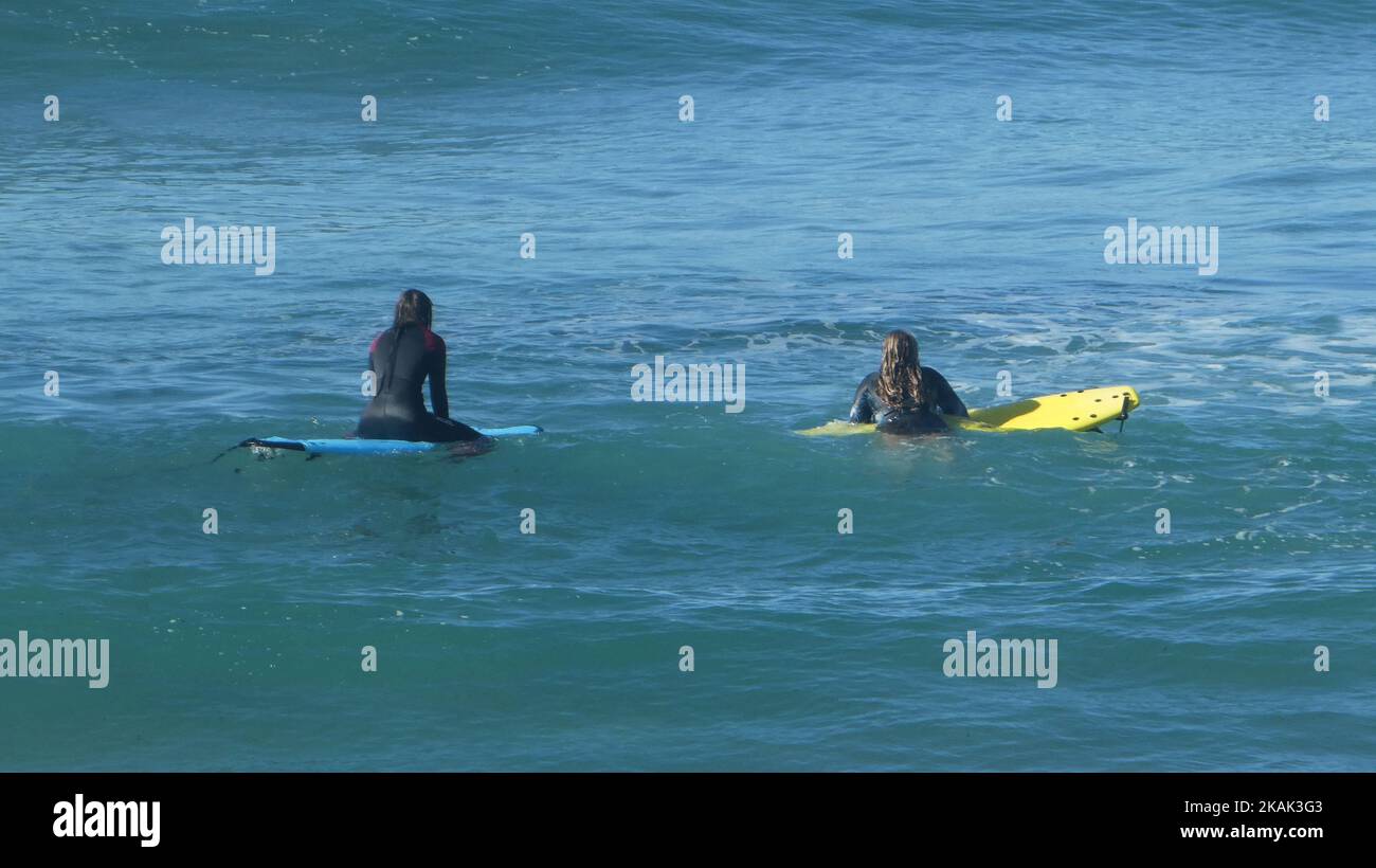 Two women wearing wetsuits floating on surfboards in the water Stock