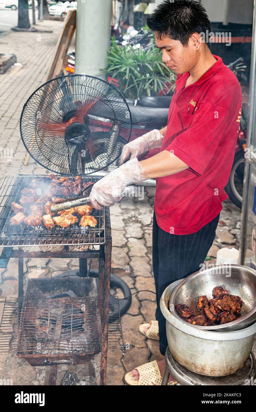 Vietnamese man cooking at roadside barbecue in street market, Ho Chi Minh City, Vietnam Stock Photo
