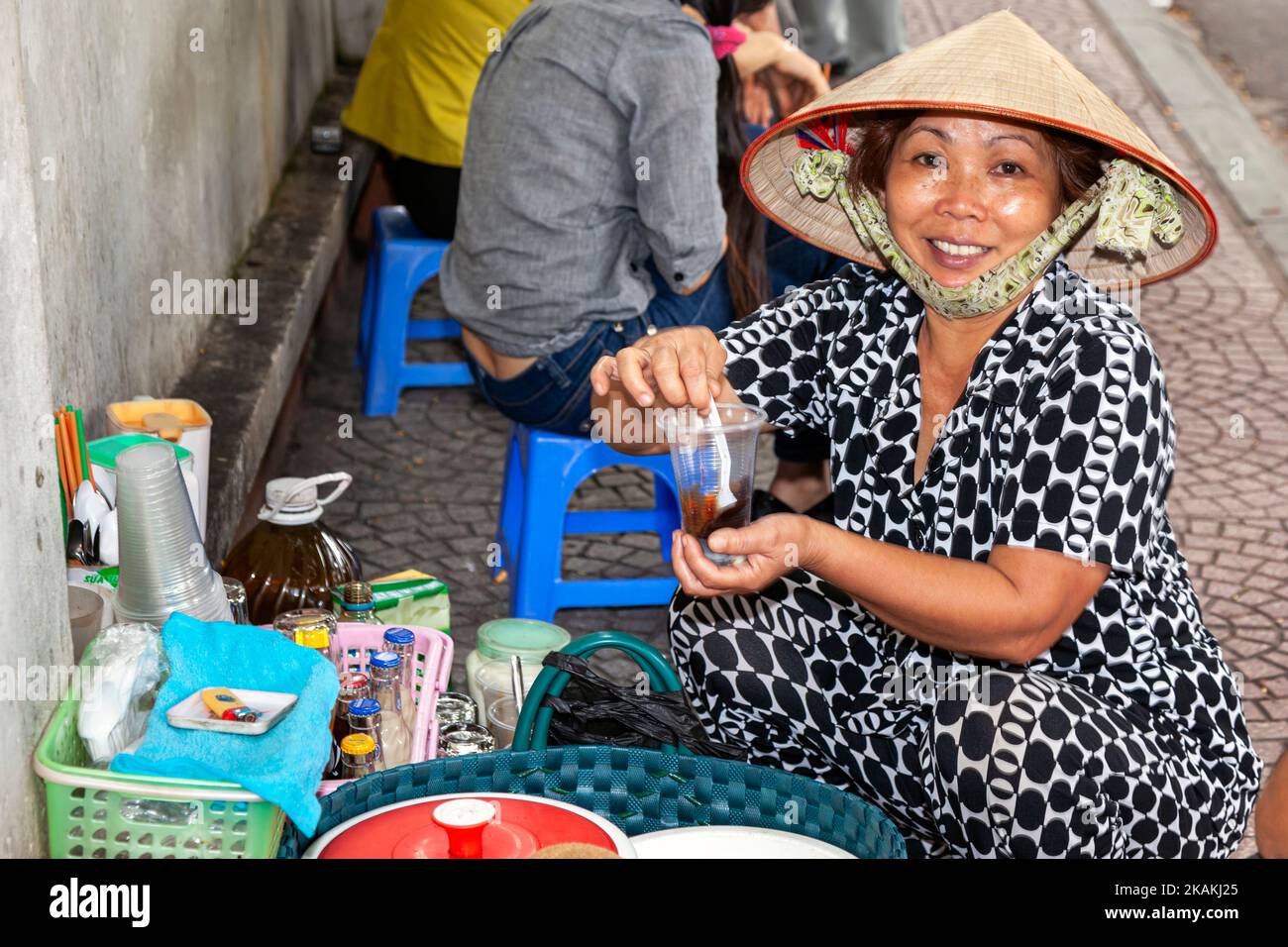 Vietnamese lady wearing bamboo hat selling coffee at pavement cafe, Ho Chi Minh City, Vietnam Stock Photo