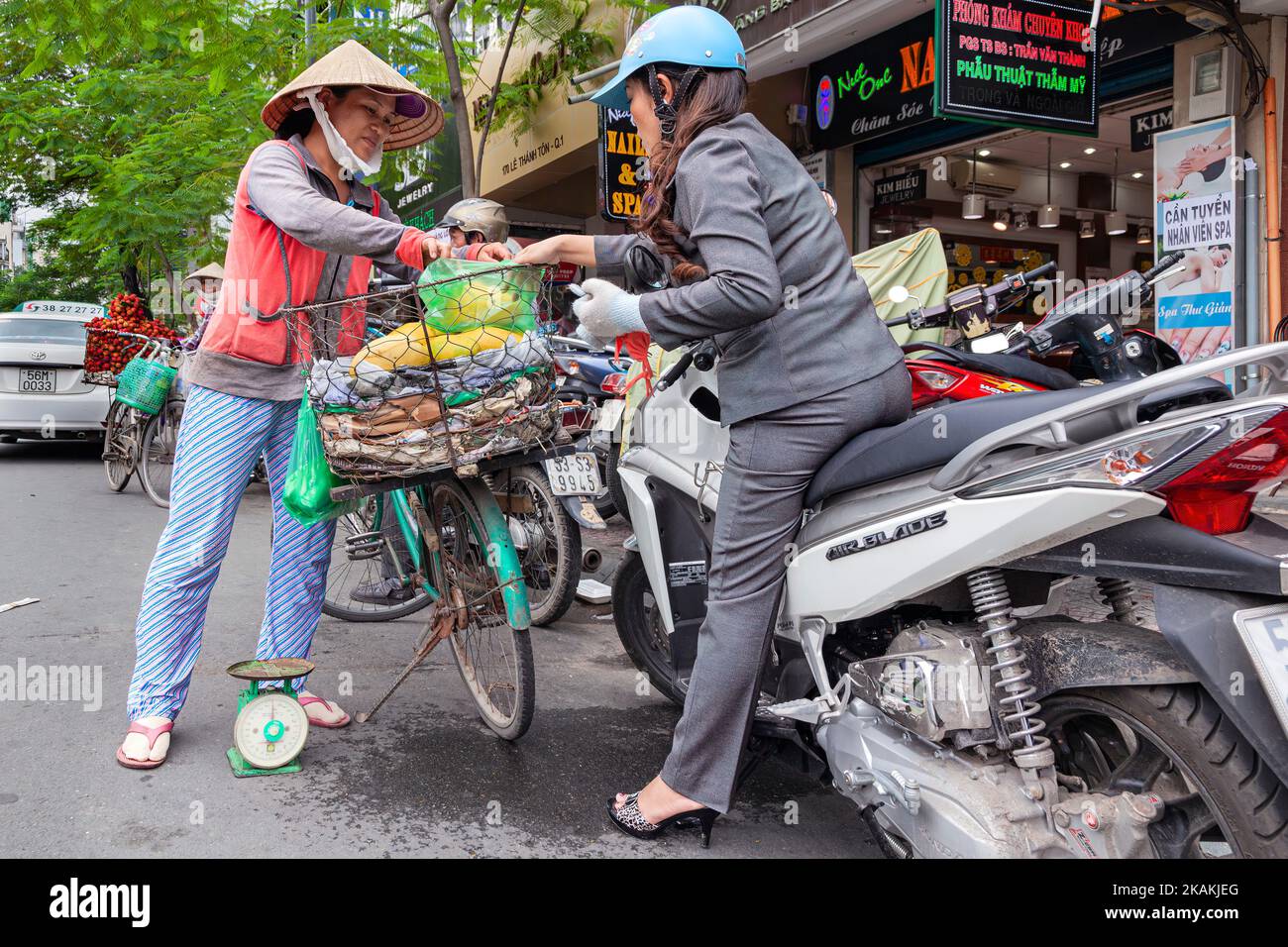 Street hawker wearing bamboo hat selling fruit to motorbike rider at roadside, Ho Chi Minh City, Vietnam Stock Photo