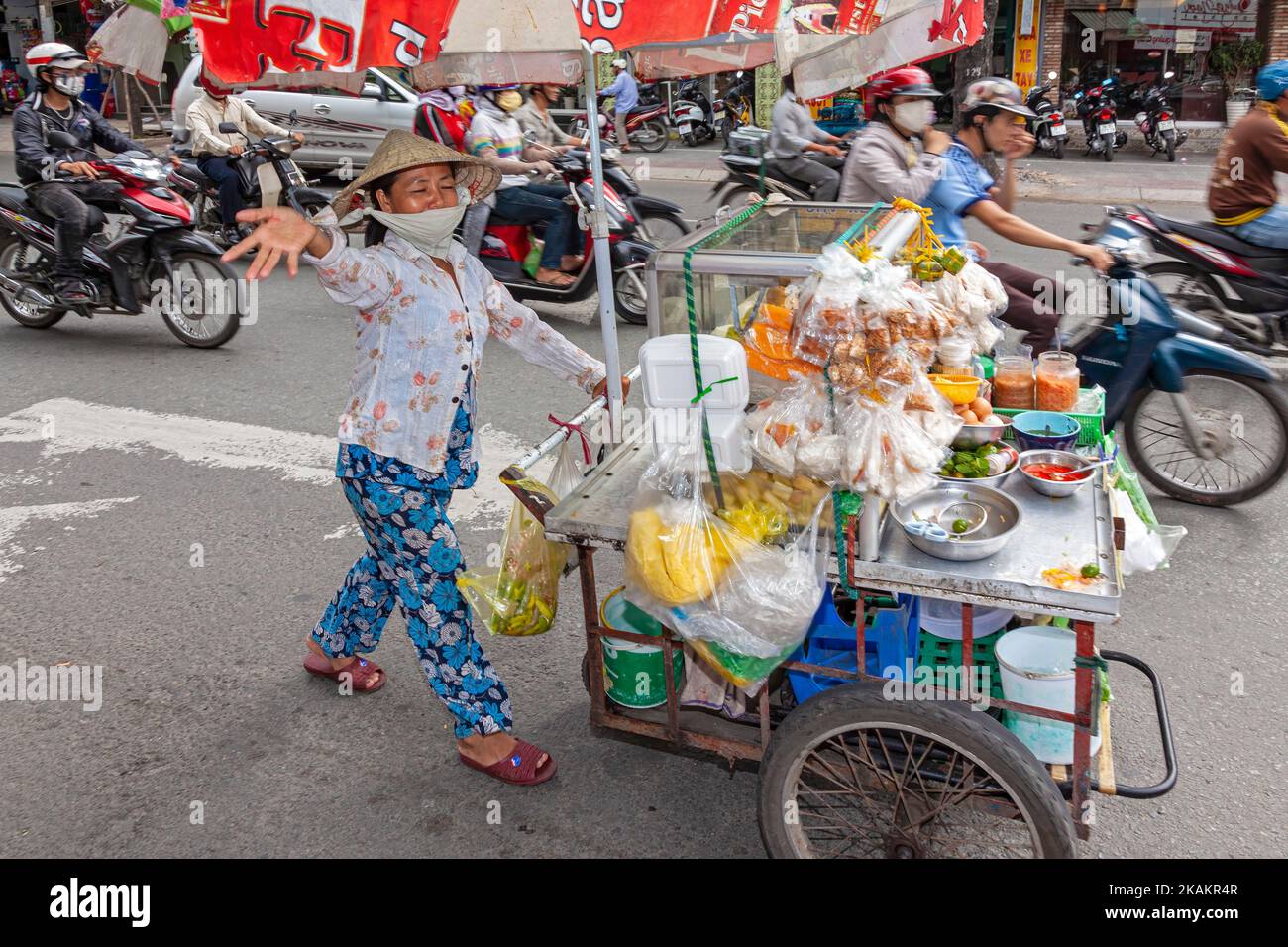 Vietnamese, lady, wearing, bamboo, hat, in, traffic, with, food, pushcart, Ho Chi Minh, City, Vietnam, cart, cook, cooking, hawker, vendor, trader, et Stock Photo
