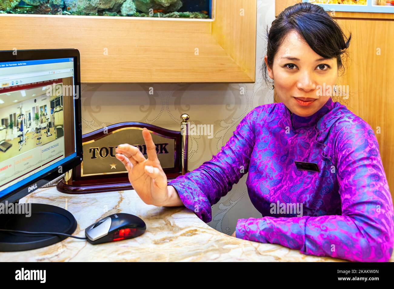 Vietnamese hotel receptionist wearing ao dai making booking on internet at tour desk, Ho Chi Minh City, Vietnam Stock Photo
