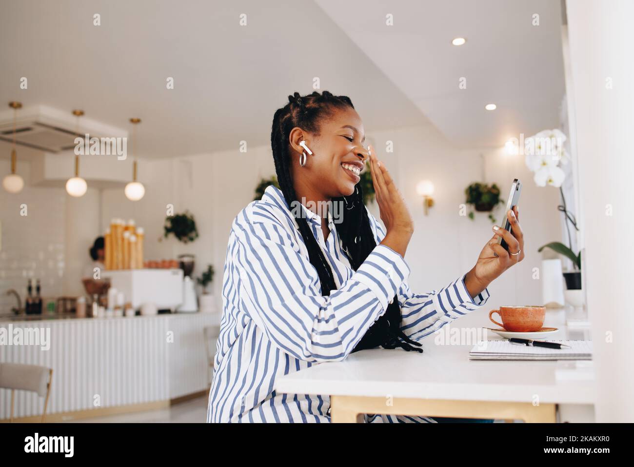 Smiling businesswoman waving a greeting on a video call while working in a cafe. Happy young black businesswoman video chatting with one of her client Stock Photo