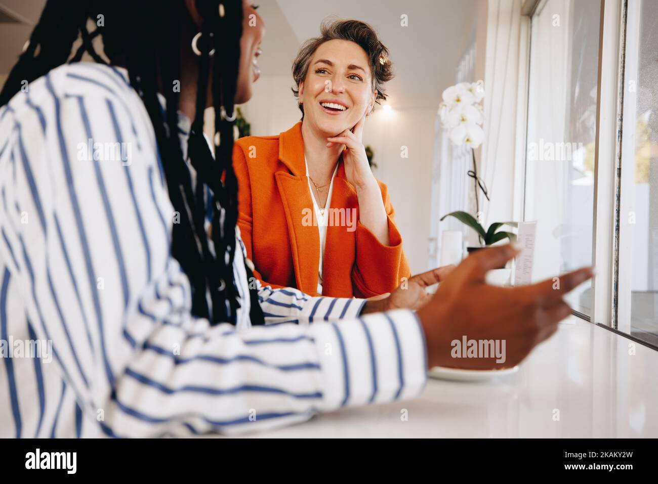 Smiling businesswomen having a discussion while sitting together in a coffee shop. Two happy female business colleagues sharing ideas during a coffee Stock Photo