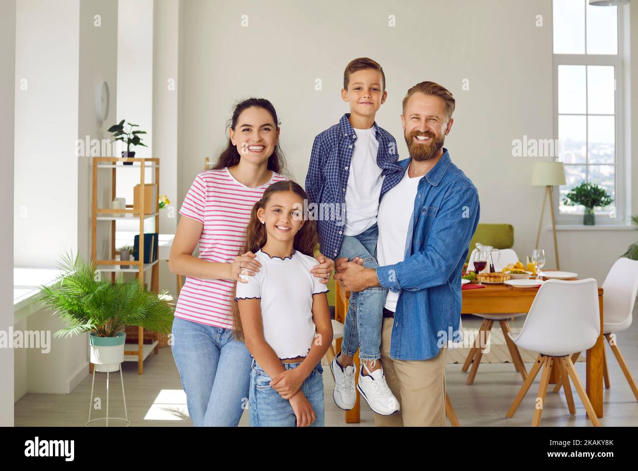 Portrait of happy family mom, dad, son and daughter in dinning room looking at camera. Stock Photo