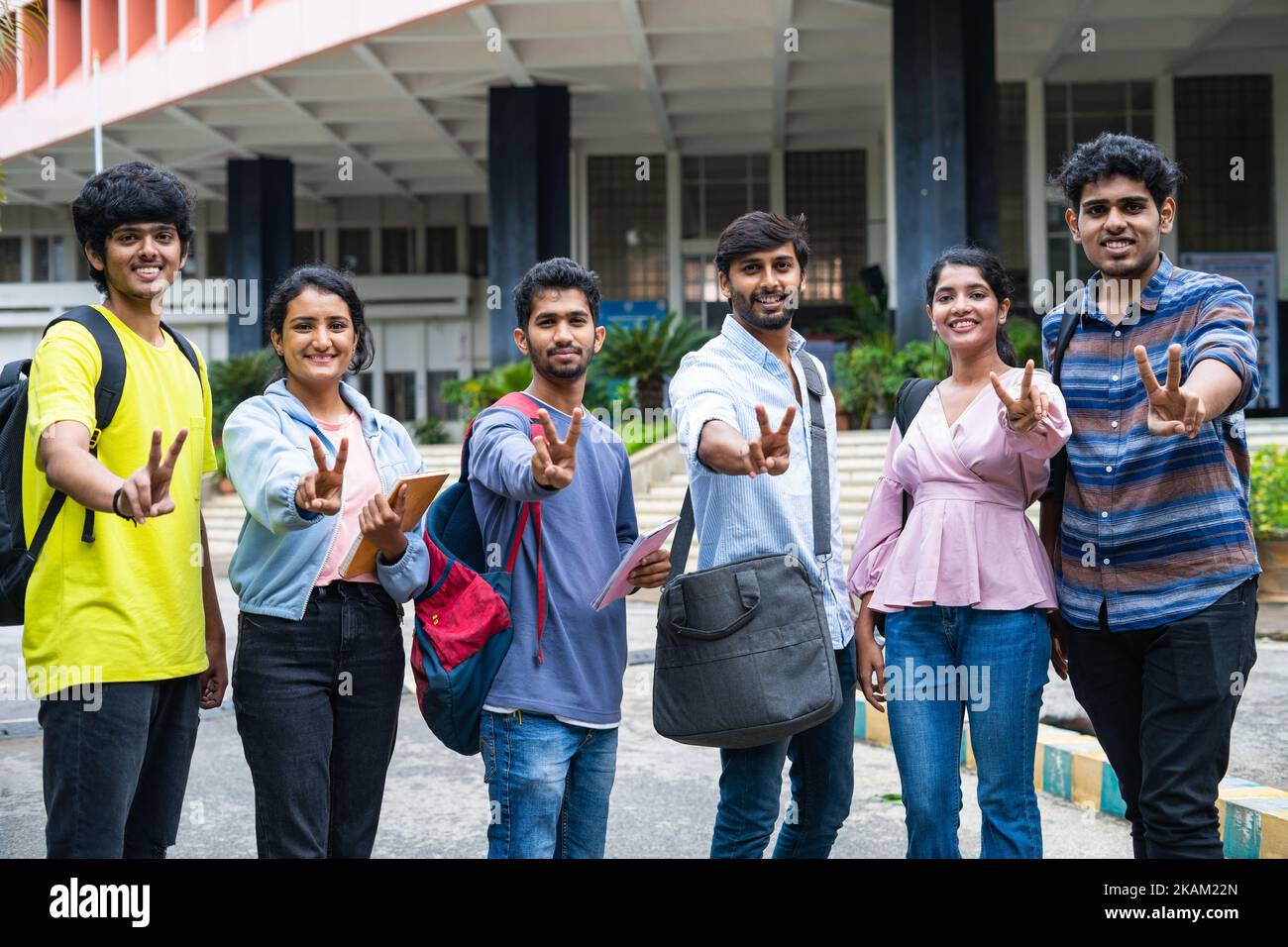 group of college students showing victory sign or gesture by looking at camera while standing at college campus - concept of successful placements Stock Photo