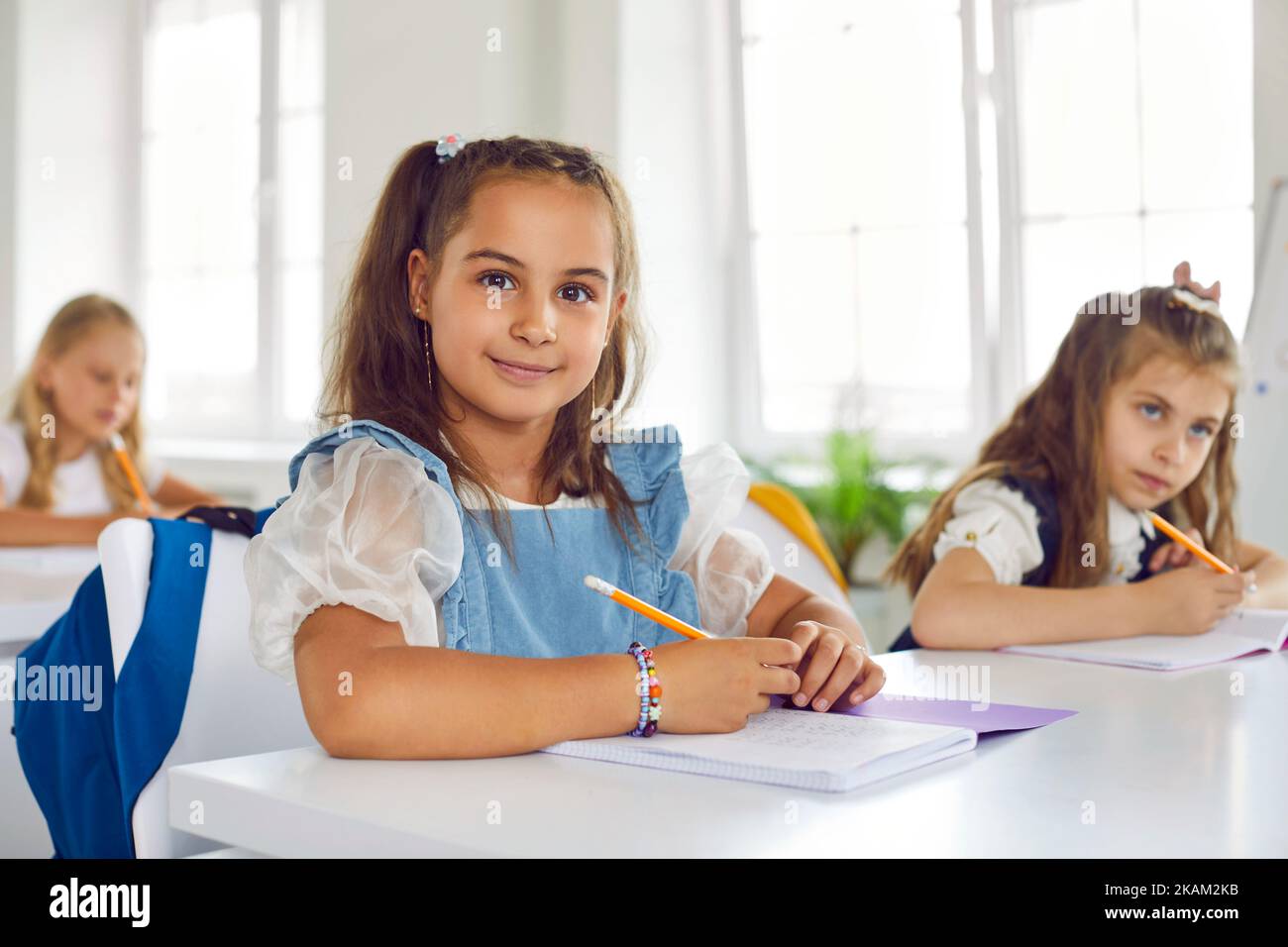 Portrait of a happy beautiful little schoolgirl sitting at her desk in the classroom Stock Photo