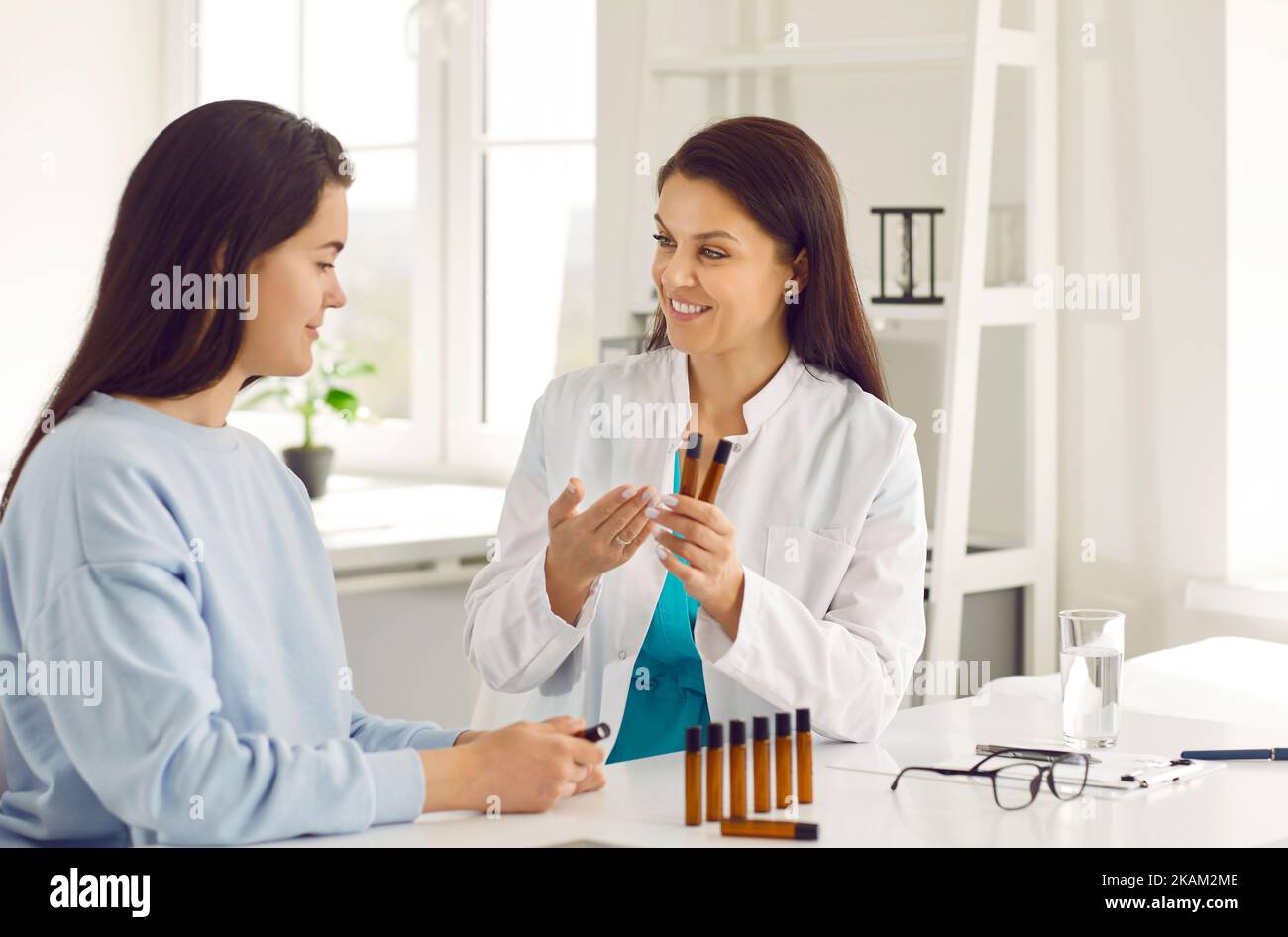 Friendly female doctor presents to young woman bottles of essential oils to improve well-being. Stock Photo