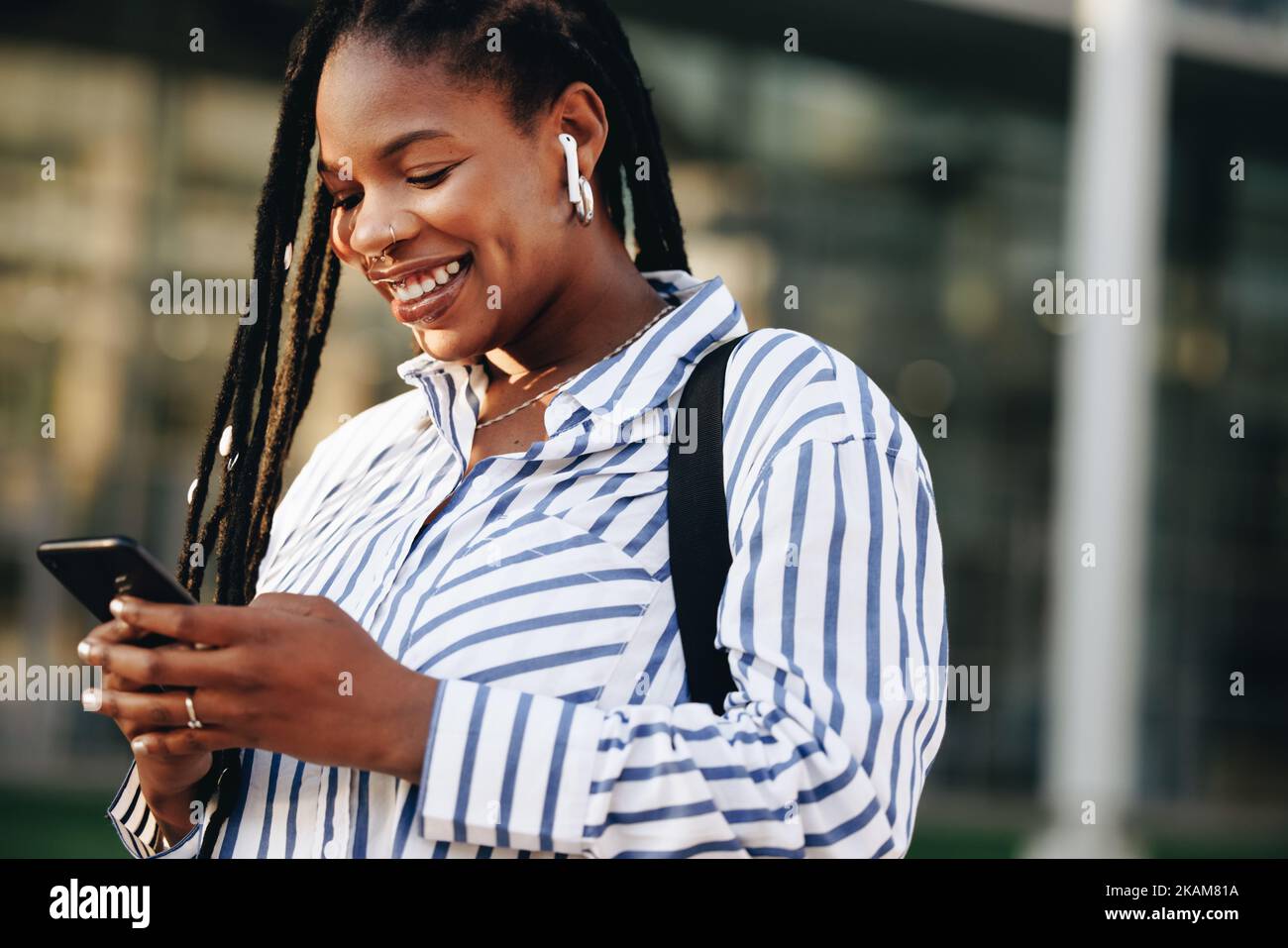 Cheerful young business woman using a smartphone on her way to work in the city. Happy young businesswoman playing music on her phone while commuting Stock Photo