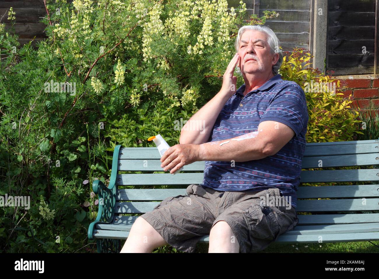 Senior or elderly man applying sun cream or blocker to his face. Sitting in the hot sun. Prevention from sunburn. Stock Photo