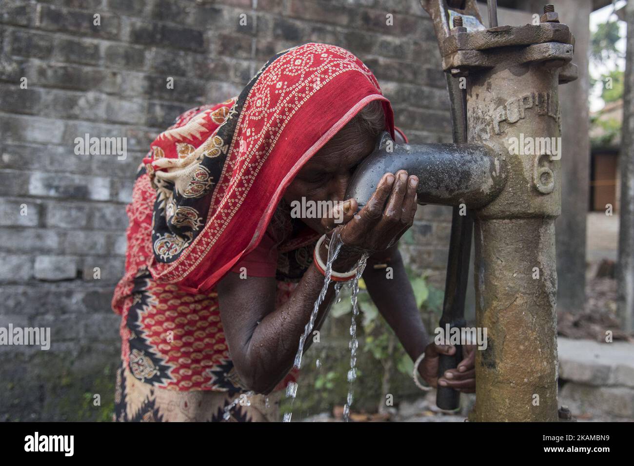 A woman is drinking water from a tube well which is left without the arsenic alert label. Gaighata, West Bengal, on India 2 April 2017. Gaighata, a village in north 24 parganas located near the Indo Bangladesh border is one of the highly arsenic affected areas of West Bengal. Almost all the water bodies of this area including tube wells produces arsenic contaminated water. Villagers are forced to use arsenic contaminated water for drinking purpose and for every other household chores. According to the WHO, drinking arsenic-rich water over a long period of time results in various health hazards Stock Photo