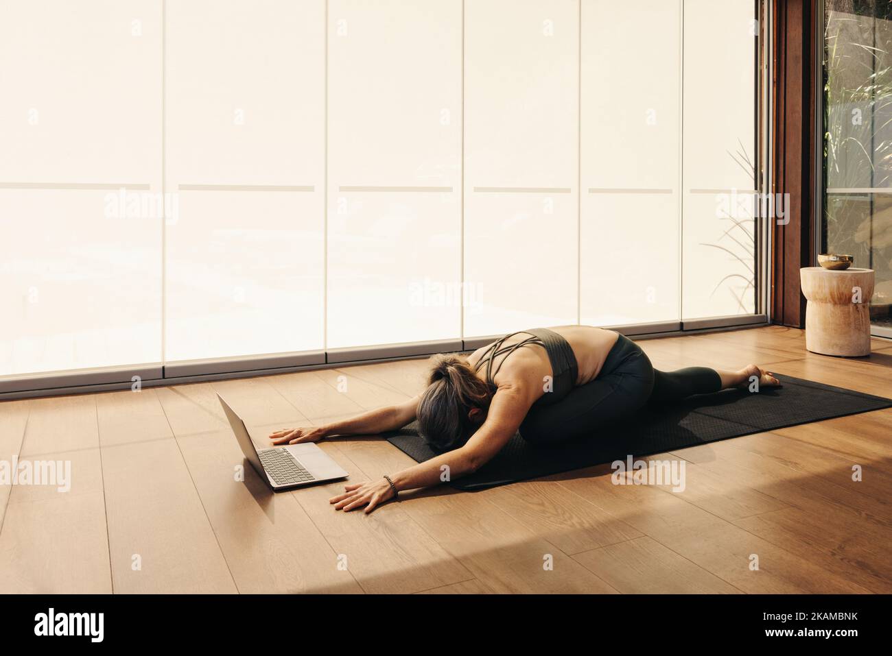 Woman doing a balasana exercise during an online yoga class at home. Mature woman practicing a kneeling asana on an exercise mat. Senior woman followi Stock Photo