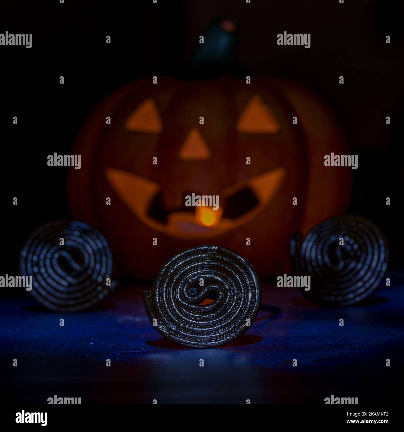 Three spirals of licorice candy with a Halloween pumpkin in the background with a light inside