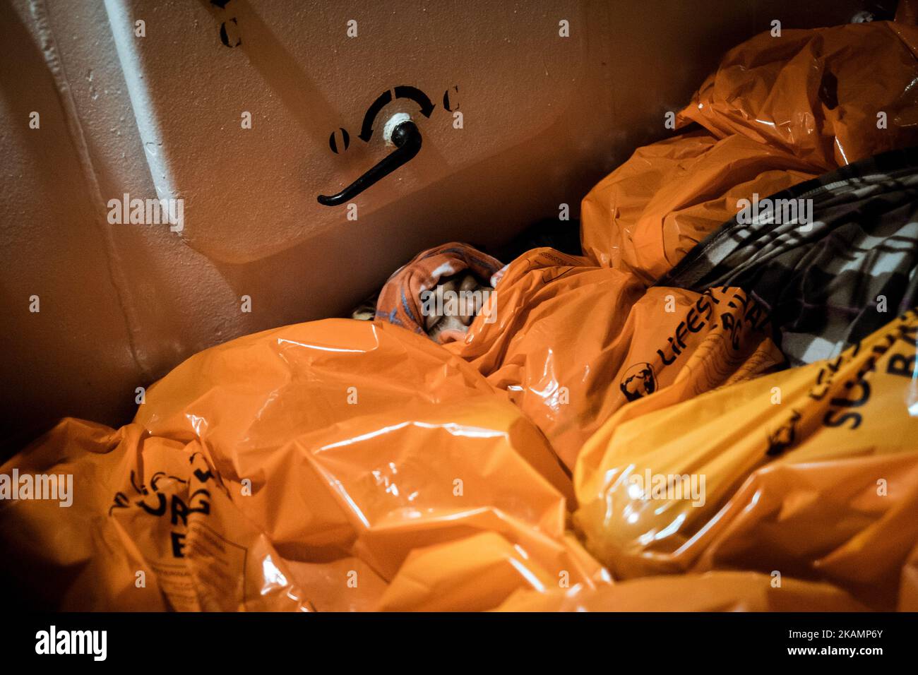 February 22nd 2017. Migrants squeezed togheter sleep on board the Aquarius squeezed togheter. Due to the low winter temperatures, the Aquarius crew provides them with orange survival bags that keep the body warm and sheltered from the wind. Pushed by numerous humanitarian crisis in Africa, Middle East and Asia, and a worsening situation of widespread violence in lawless Libya, the exodus towards Europe through the Mediterranean continues even during the coldest months of the year. From January to March 2017 alone, 602 people lost their lives at sea. The migrants’ ordeal in Libya and during the Stock Photo