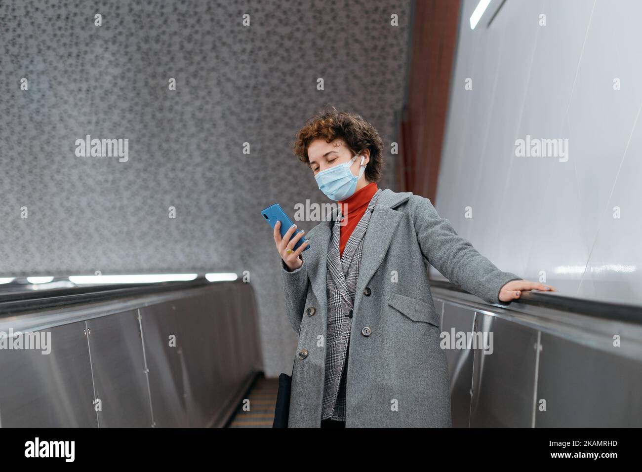 woman in a protective mask standing on the escalator steps in the ...