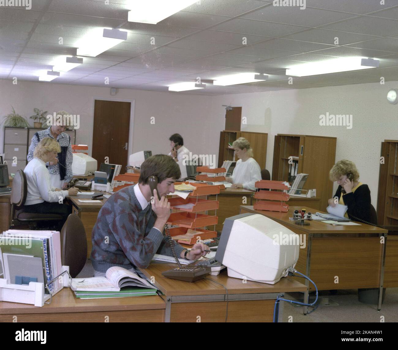 1989, historical, open plan office, male & female employees working at desks, some on the telephone, England, UK using computer consoles or PCs of the era. It was in the early 80s, when IBM launched its PC, that the small desktop personal computer market really began. Stock Photo
