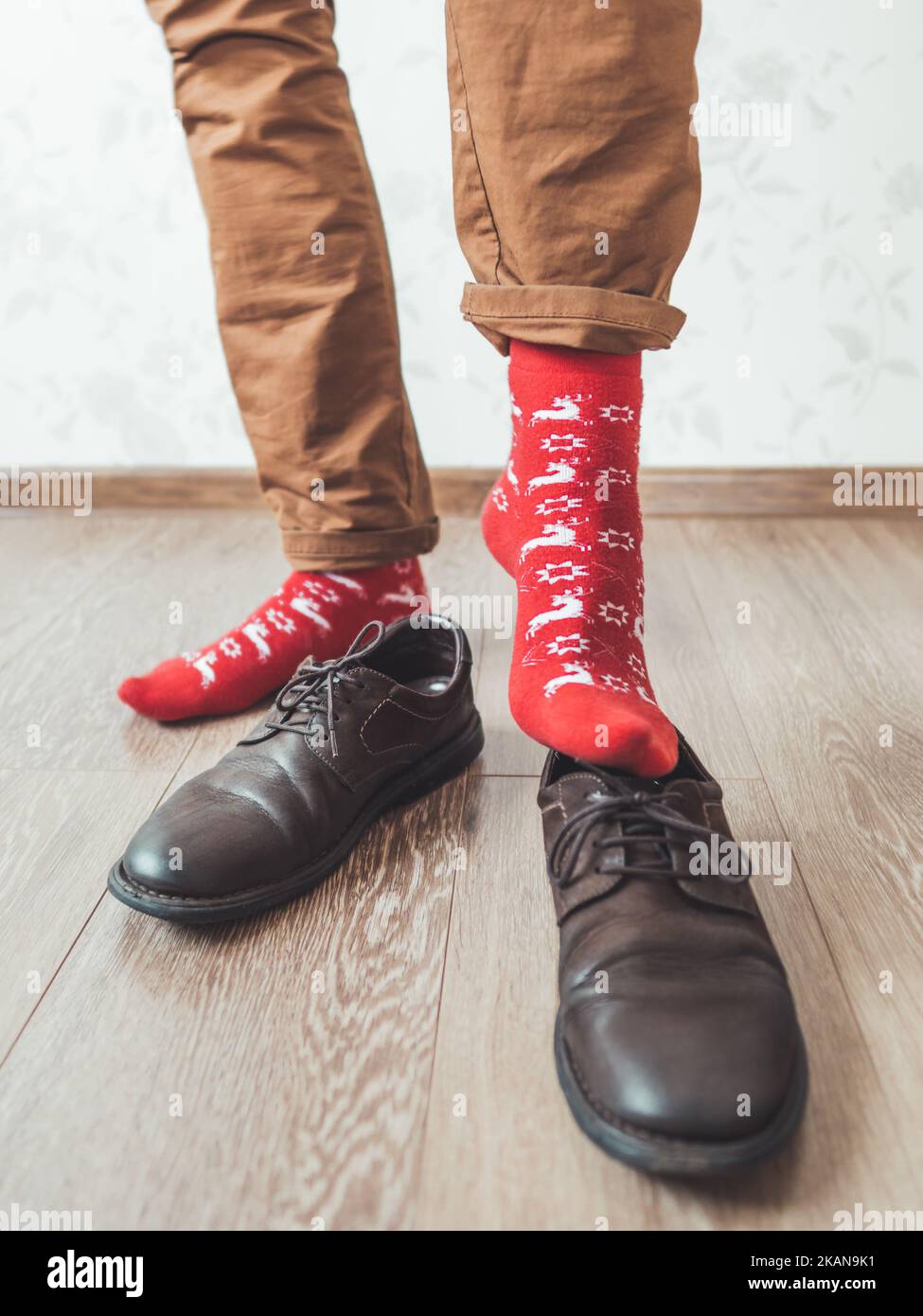 Young man in chinos trousers and bright red socks with reindeers on them is ready to wear suede shoes. Scandinavian pattern. Winter holiday spirit. Ca Stock Photo