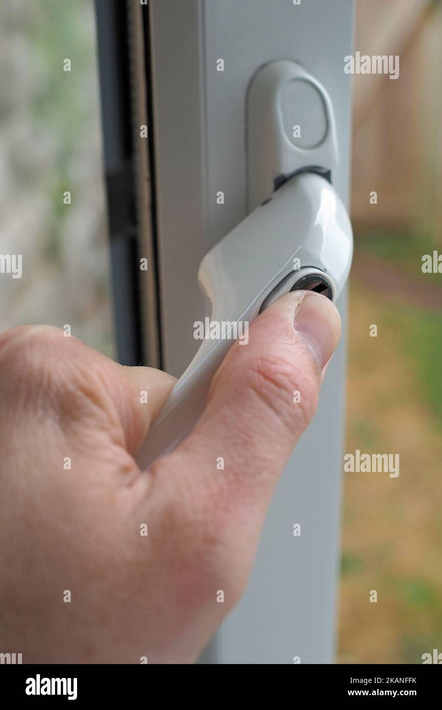 A vertical shot of a white window lock with a handle on a PVC window ...