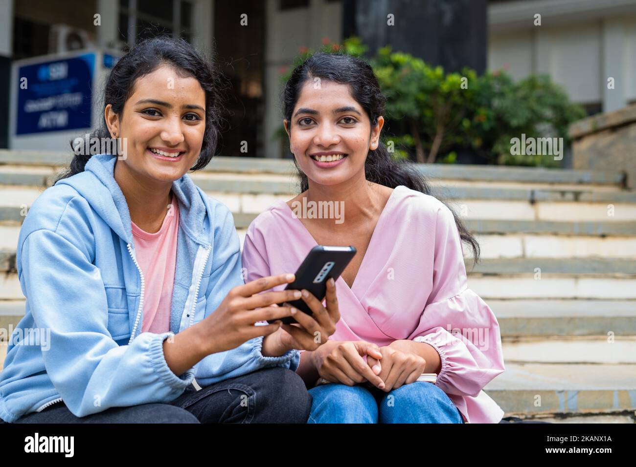 Happy smiling students looking at camera while using mobile phone at college campus showing with copy space - concept of technology, education and Stock Photo