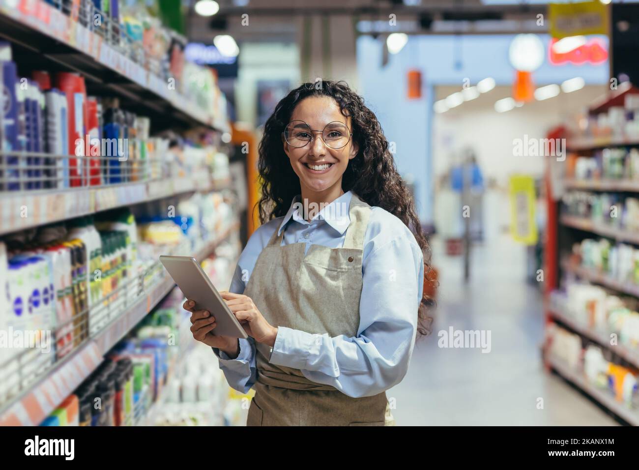 Portrait of happy and successful saleswoman, hispanic woman with curly hair smiling and looking at camera, using tablet computer to review product. Stock Photo