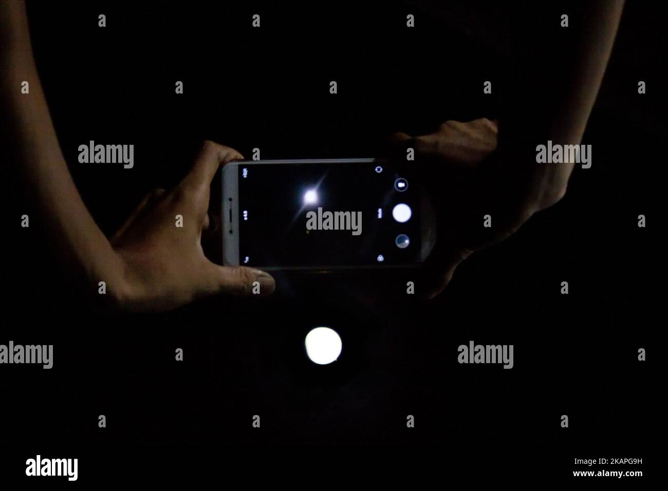 Peoples try to capturing pictures of partial lunar eclipse phenomenon by mobile phone camera at Cibitung District, West Java on Monday, August 7, 2017. Tonight, the moon experiences a partial eclipse phenomenon with a duration of 5 hours 4.9 minutes, which begins on Monday, August 7 at 10:48 pm local time till Tuesday, August 8 at 3:52 am local time, while the peak of a partial lunar eclipse occurs at 1:20 local time. According to information published by the Indonesian Meteorology, Climatology and Geophysics Agency, the phenomenon of partial lunar eclipses today is the 61st member of 80 membe Stock Photo