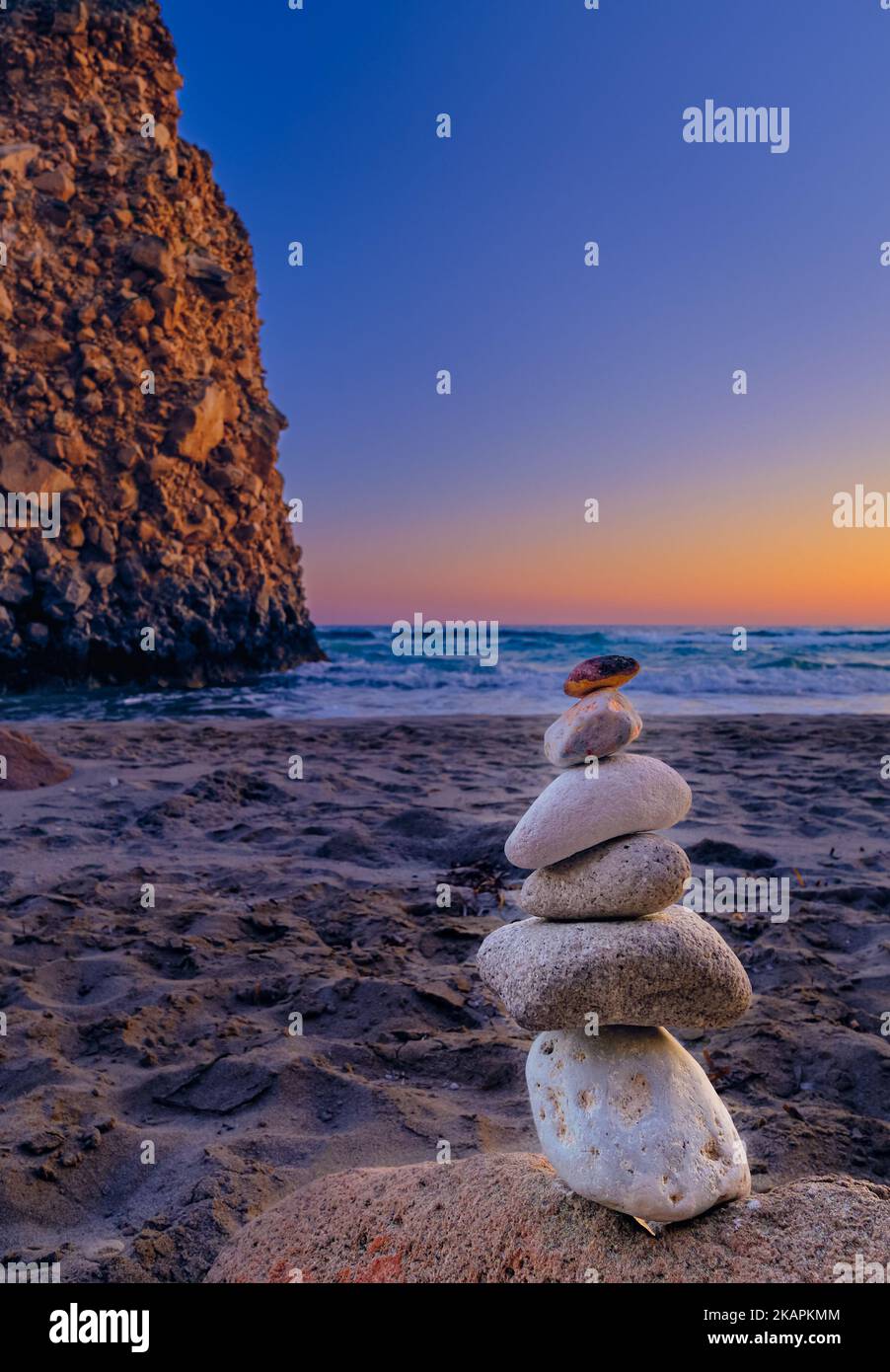 Balance stone stack and big natural rock on sandy beach at sunset.  Stock Photo
